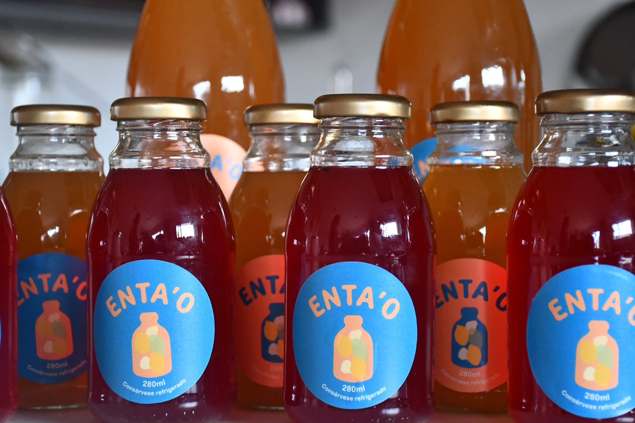 Fila de botellas de kéfir Enta'o de 280ml, unas de mora rojas y otras de maracuyá ámbar, con etiquetas azules y naranjas.