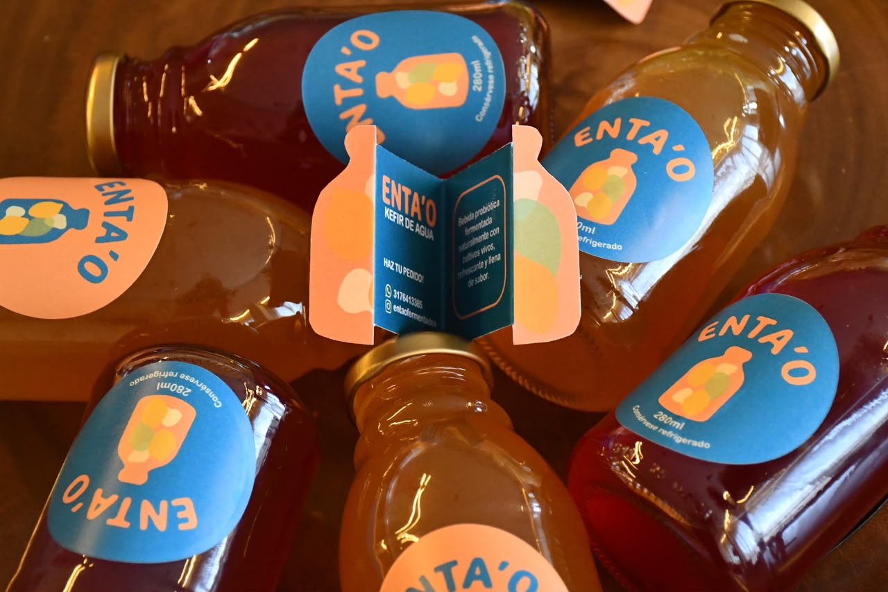 Botellas de kéfir Enta'o vistas desde arriba sobre una mesa de madera, alrededor de una tarjeta plegable de la marca.
